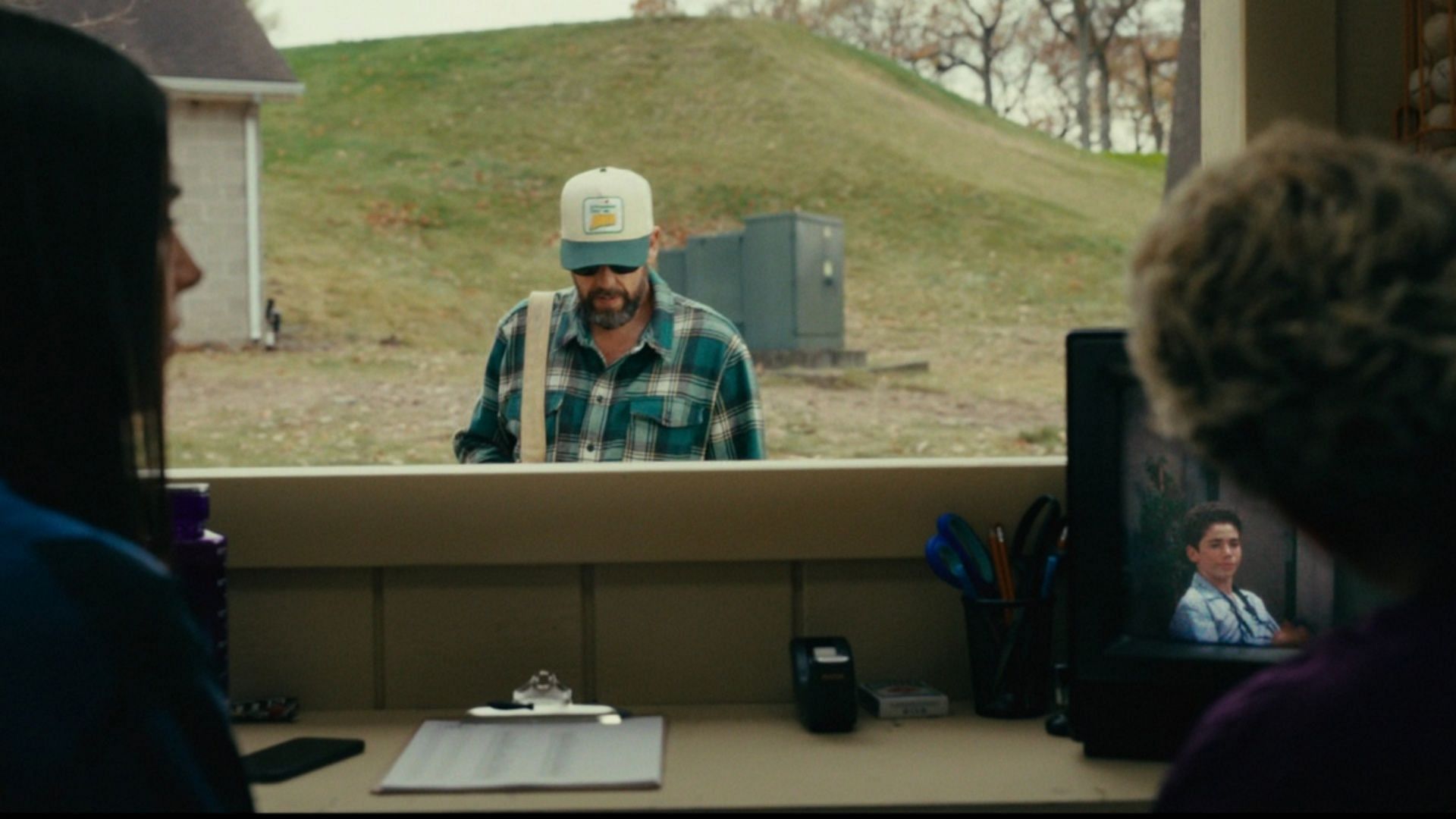 A scene from Happy Gilmore 2 shows Adam Sandler’s character approaching a check-in booth while a clip from Disney Channel’s Jessie, featuring Cameron Boyce as Luke Ross, quietly plays on a CRT television in the background, a subtle tribute to the late actor. (Image via Netflix)